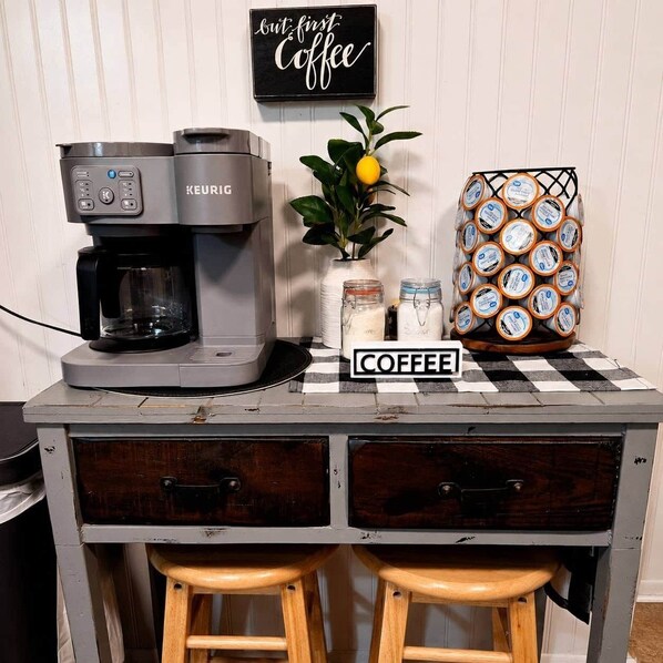 A coffee station with a Keurig coffee maker, a coffee-themed sign, a jar of sugar, a jar of cream, and a basket of coffee pods. - Waggoner in Longview (Longview)