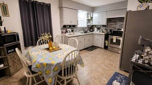 A compact kitchen with white cabinets, a dining table with chairs, a refrigerator, and a microwave. - Waggoner in Longview (Longview)