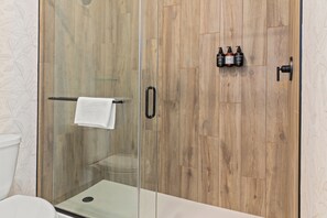 A modern bathroom with a glass shower enclosure, wooden panel walls, and a visible toilet. - The Wills Hotel (Cumberland)