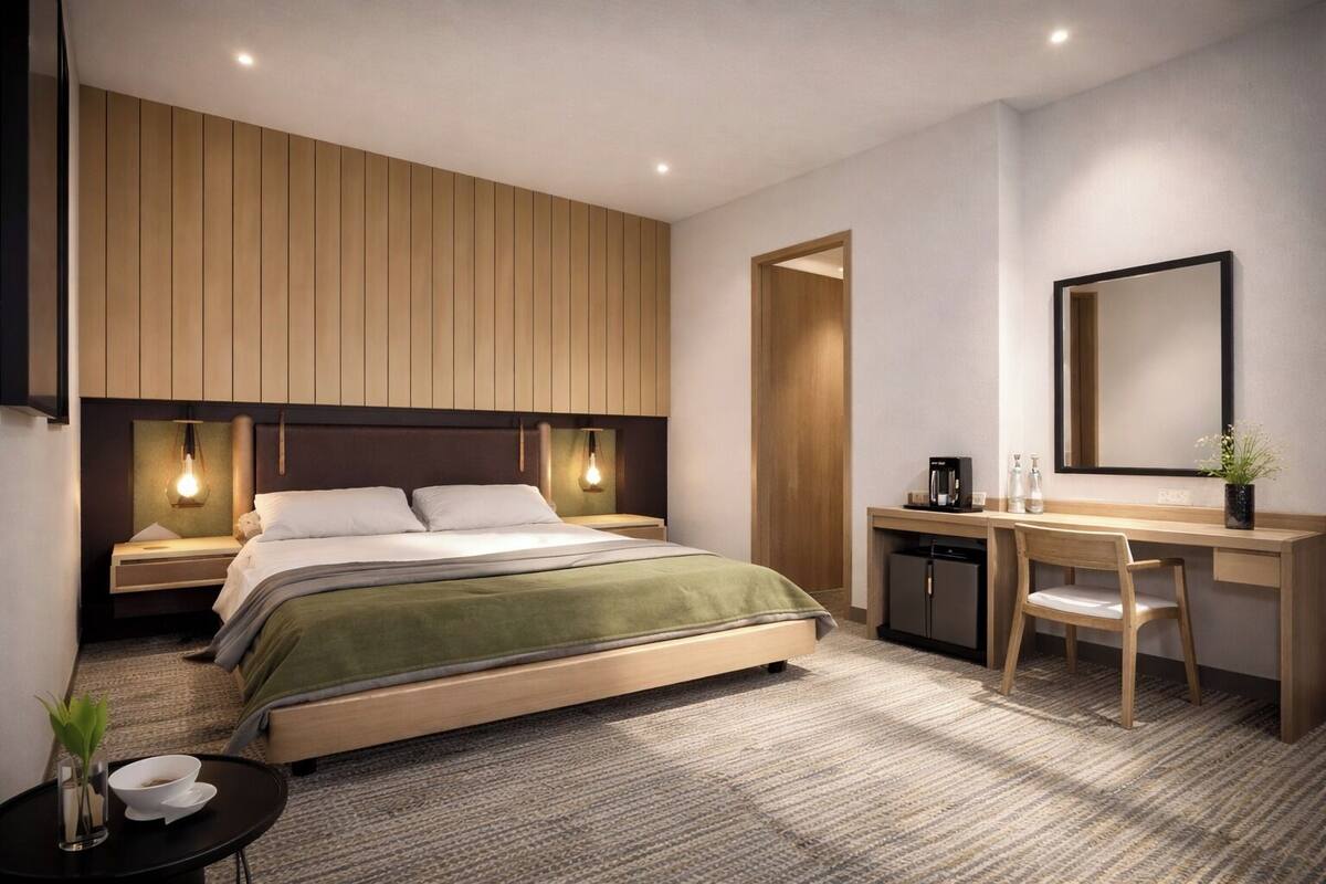 A modern hotel room with a bed, bedside tables, a desk, a chair, a mirror, and a small plant.