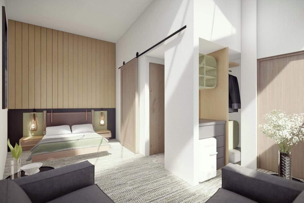 A modern bedroom with a bed, bedside tables, a wardrobe, and a small sitting area with a sofa and a vase of flowers.