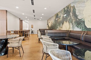 A restaurant with a wooden floor, white wicker chairs, a brown leather booth, and a large wall mural. - The Wills Hotel (Cumberland)