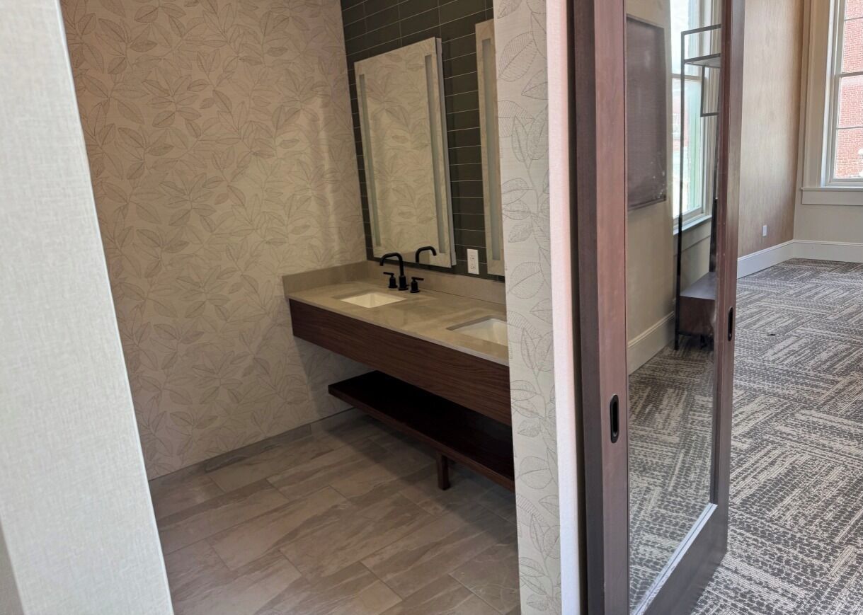 A bathroom with a wooden vanity, a mirror, and a patterned wall.
