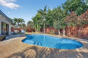 Une piscine à bord incurvé, entourée d’une clôture en bois et de différents arbres.
