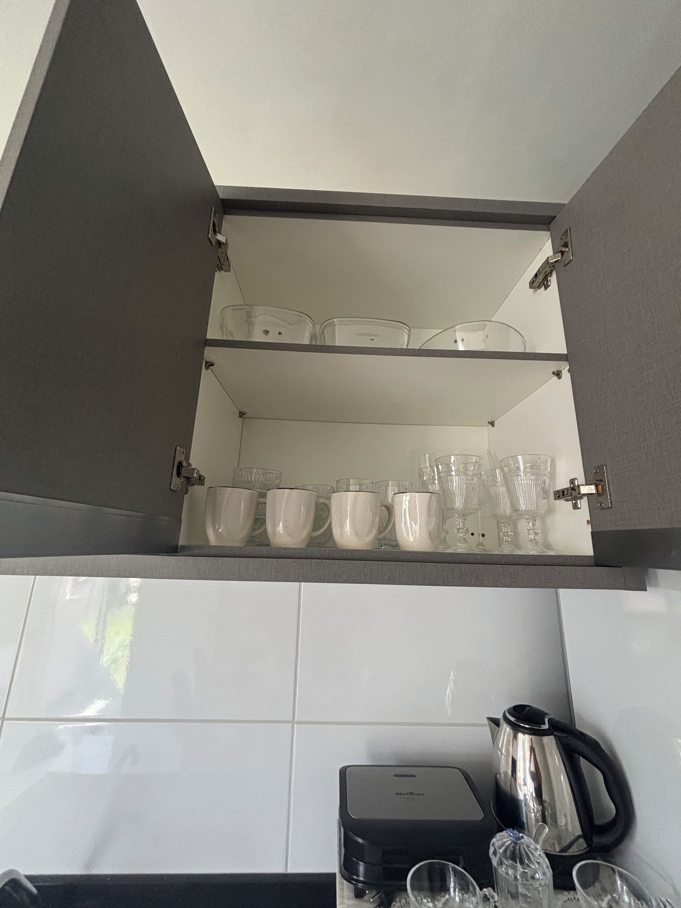 Ein Küchenschrank mit drei Einlegeböden, auf denen klare Glasbecher und Schüsseln stehen.