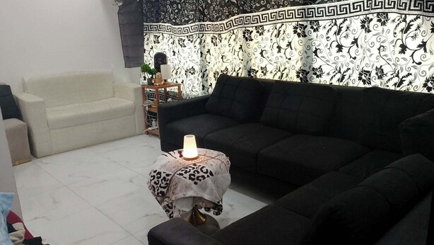 Uma sala de estar com um sofá bege, um sof á preto e uma mesa redonda pequena com abajur.