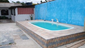 Uma piscina com borda azulejada, parede azul e um edifício branco com parede de fundo estampada em vermelho.