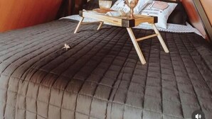 Um quarto de loft aconchegante, com teto inclinado, uma cama com estrutura de madeira e uma pequena mesa com uma xícara e um livro.