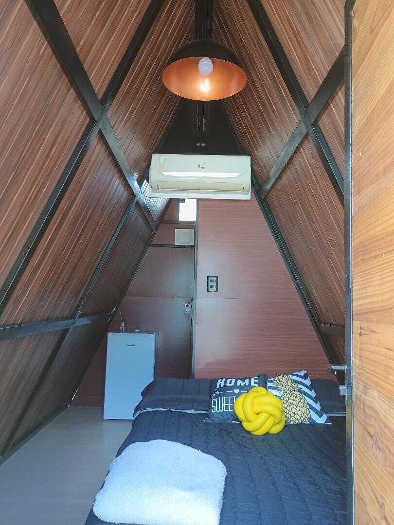 Un pequeño dormitorio abuhardillado con techo inclinado, una cama con almohada, un mueble blanco pequeño y un calentador.