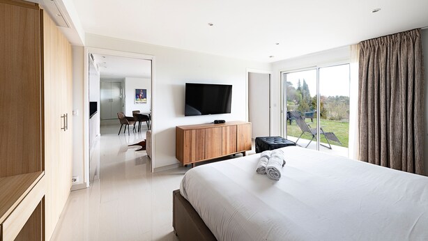 Quarto de hotel moderno com uma cama grande, televisão de tela plana, móvel de madeira e vista para o exterior.