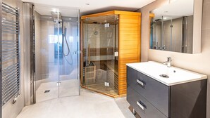 Uma casa de banho moderna com chuveiro envolto em vidro, toucador de madeira e um espelho grande.