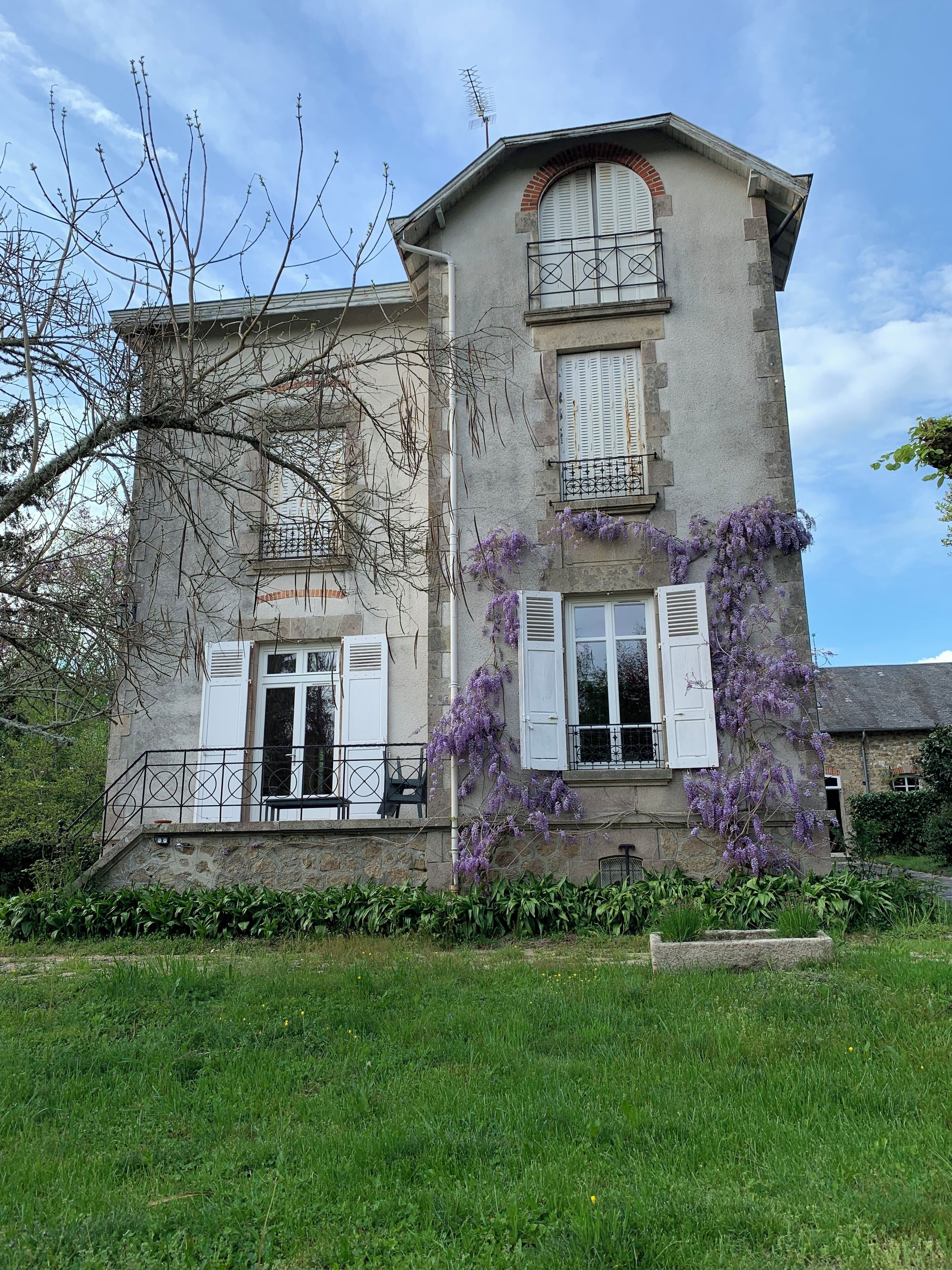 A two-story building with a stone facade, white shutters, and a balcony with a metal railing.