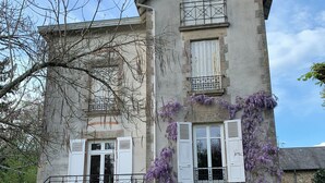 A two-story building with a stone facade, white shutters, and a balcony with a metal railing. - Beautiful country house on the edge of a village, ideal for families! (Compreignac)