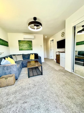 A living room with a sofa, a coffee table, a TV, and a kitchen area. -  
Charming Cozy Suite in Poway with Sloped Ceiling & Private Balcony (Poway)