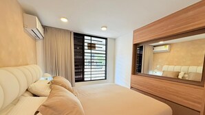 Una habitación de hotel moderna con una cama grande, un cabecero de madera, un equipo de aire acondicionado, una ventana con persianas y un espejo sobre la cama.