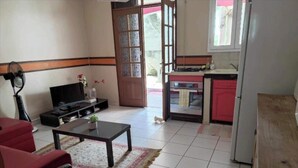 A living room with a TV, a sofa, a coffee table, and a kitchen area with cabinets and a refrigerator. - Appartement Hibiscus - Ground floor (Le Moule)