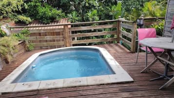 Un bain à remous sur une terrasse en bois, avec une clôture en bois et de la verdure en arrière-plan.