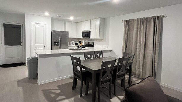 A modern kitchen with white cabinets, a stainless steel refrigerator, and a microwave. There is a dining area with a table and chairs. - Brand New Cozy 3 BD w/Fiber optic nested in quite Cul De SAC. Ultra modern (Conroe)
