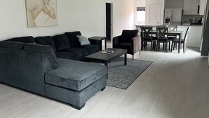 A modern living room with a grey sofa, a coffee table, and a dining area with a table and chairs. - Brand New Cozy 3 BD w/Fiber optic nested in quite Cul De SAC. Ultra modern (Conroe)