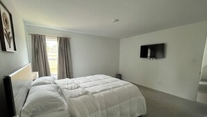 A bedroom with a bed, a TV mounted on the wall, and a window with curtains. - Brand New Cozy 3 BD w/Fiber optic nested in quite Cul De SAC. Ultra modern (Conroe)
