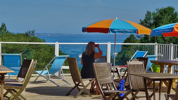 Una terraza con sillas y mesas de madera, con vista a un cuerpo de agua con barcos.