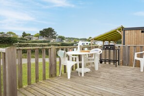 A wooden deck with a table and chairs, a grill, and a covered area. - Cap - Confort 1 - 3p (Plouézec)