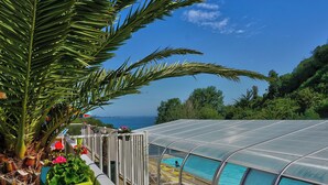 Zona de piscina con cerramiento de vidrio, rodeada de abundante vegetación y vistas al mar.