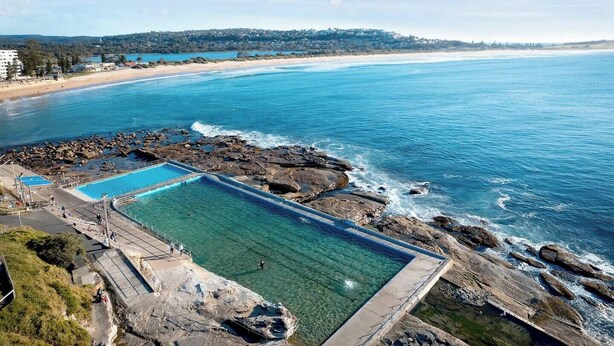 A coastal swimming pool with clear blue water, surrounded by rocky terrain and a beach in the background. - Shoreleaf Haven Moments from Waves and Seaside Eats (Dee Why)