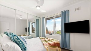A hotel room with a bed, a television, a window with curtains, and a city view. - Shoreleaf Haven Moments from Waves and Seaside Eats (Dee Why)
