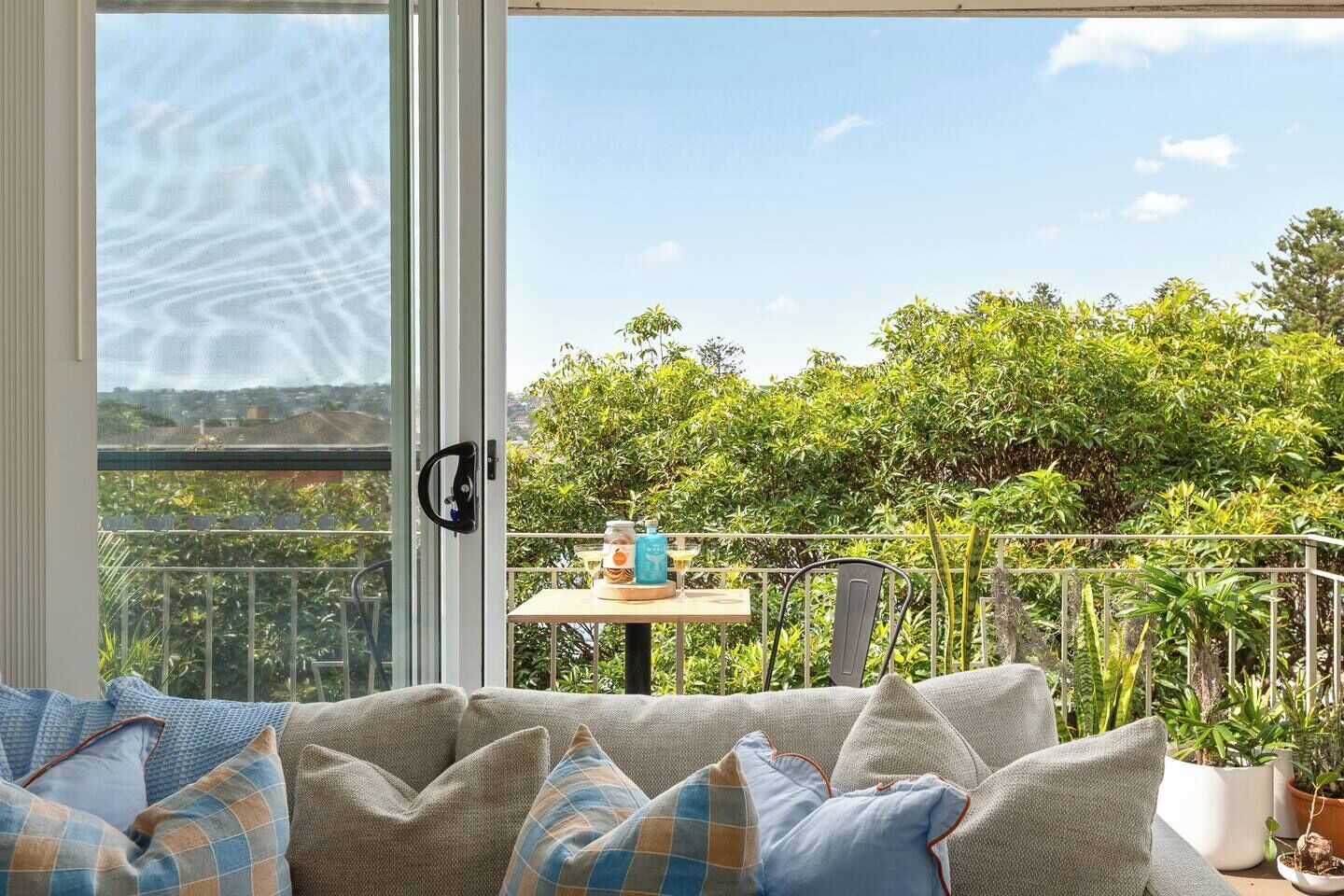 Un balcon avec un canapé, une table avec des boissons et des plantes en pot.