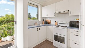 A modern kitchen with white cabinets, a built-in oven, and a window overlooking greenery. - Shoreleaf Haven Moments from Waves and Seaside Eats (Dee Why)