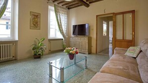 A living room with a sofa, a glass coffee table, a TV, a cabinet, a potted plant, and a door. - Casa San Girolamo, historic flat with terrace in Lucca's City Center (Lucca)