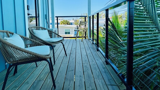 Una terraza de madera con sillas de mimbre y vista a un edificio a través de una ventana.