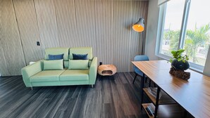 Una sala moderna con un sofá verde, una mesita redonda con una planta y suelo de madera.