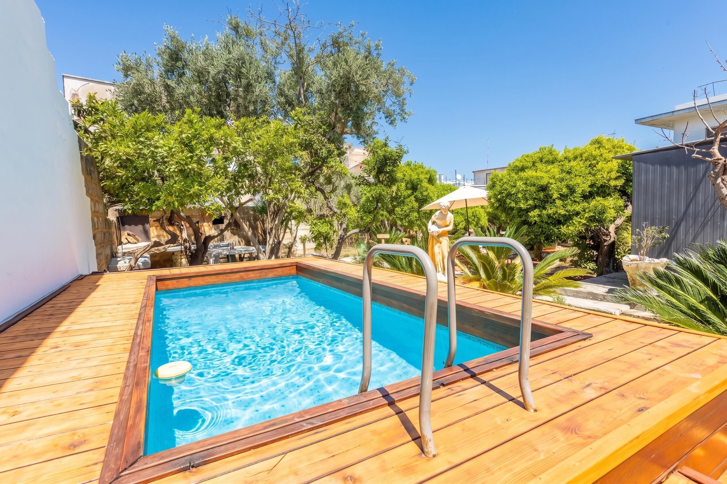 A rectangular swimming pool with a wooden deck, metal pool ladder, and a statue.