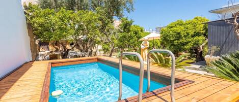 A rectangular swimming pool with a wooden deck, metal pool ladder, and a statue.