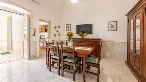 A dining area with a wooden table and chairs, a vase with flowers, a television, and a cabinet. - Villa Levante - Taviano (Taviano)