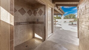 A shower area with a handrail, a door with a 'No Bare Feet' sign, and a view of an outdoor patio with a pool and desert landscaping. - Spacious Catalina Mountain View Retreat 30+ min (Tucson)
