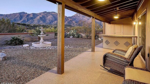 A covered outdoor patio with a stone floor, a wicker chair, and a fountain. - Spacious Catalina Mountain View Retreat 30+ min (Tucson)