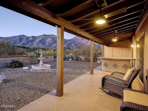 A covered outdoor patio with a stone floor, a wicker chair, and a fountain. - Spacious Catalina Mountain View Retreat 30+ min (Tucson)