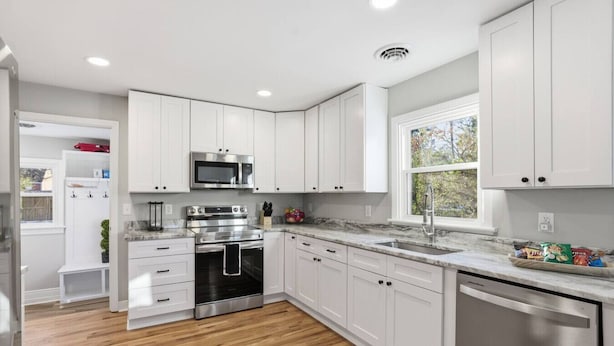 Una cocina moderna con armarios blancos, electrodomésticos de acero inoxidable y piso de madera.
