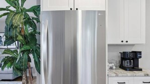 Un refrigerador de acero inoxidable con dos puertas, armarios blancos y una cafetera sobre la encimera.