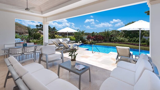 A covered outdoor area with white lounge chairs, a pool, and umbrellas. - 4 bed Prestigious Luxury Villa, Royal Westmoreland (Lancaster)