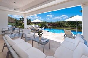 Un espacio exterior cubierto con sillones blancos, una piscina y sombrillas.