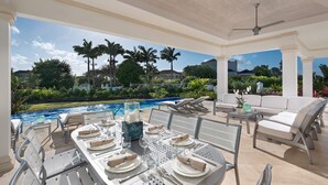 A covered outdoor dining area with a pool view, white furniture, and a neatly set table. - 4 bed Prestigious Luxury Villa, Royal Westmoreland (Lancaster)