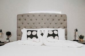 Una cama bien tendida con ropa blanca y dos almohadas a lunares negros y blancos.