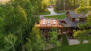 A multi-story wooden cabin with a deck, surrounded by dense forest. - Elegant Elite Estate — Wedding Venue w/ Lodging (Pigeon Forge)
