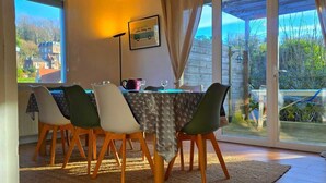 Un coin repas avec une table dressée pour quatre personnes, un luminaire suspendu et une vue sur l’extérieur grâce à de grandes portes-fenêtres coulissantes.