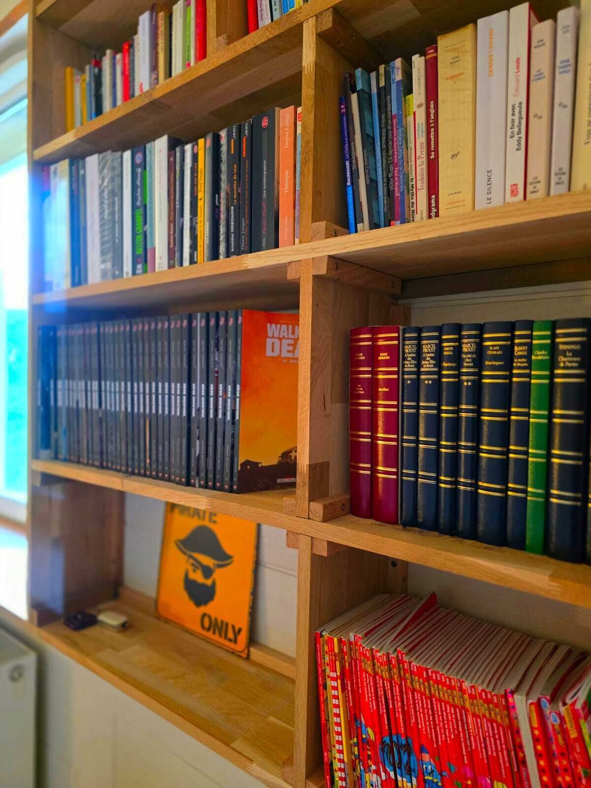 Une bibliothèque remplie de divers livres, un panneau indiquant « À UTILISER UNIQUEMENT SUR LE MUR », et une rangée de livres colorés sur l’étagère inférieure.