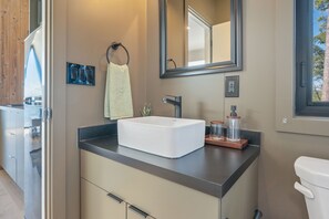 Ein modernes Badezimmer mit einem weißen Waschbecken, einem großen Spiegel und einem Fenster.